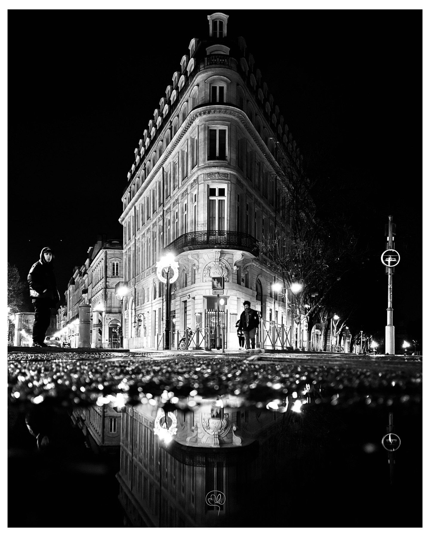 An illuminated Bordeaux building reflected on wet ground at night