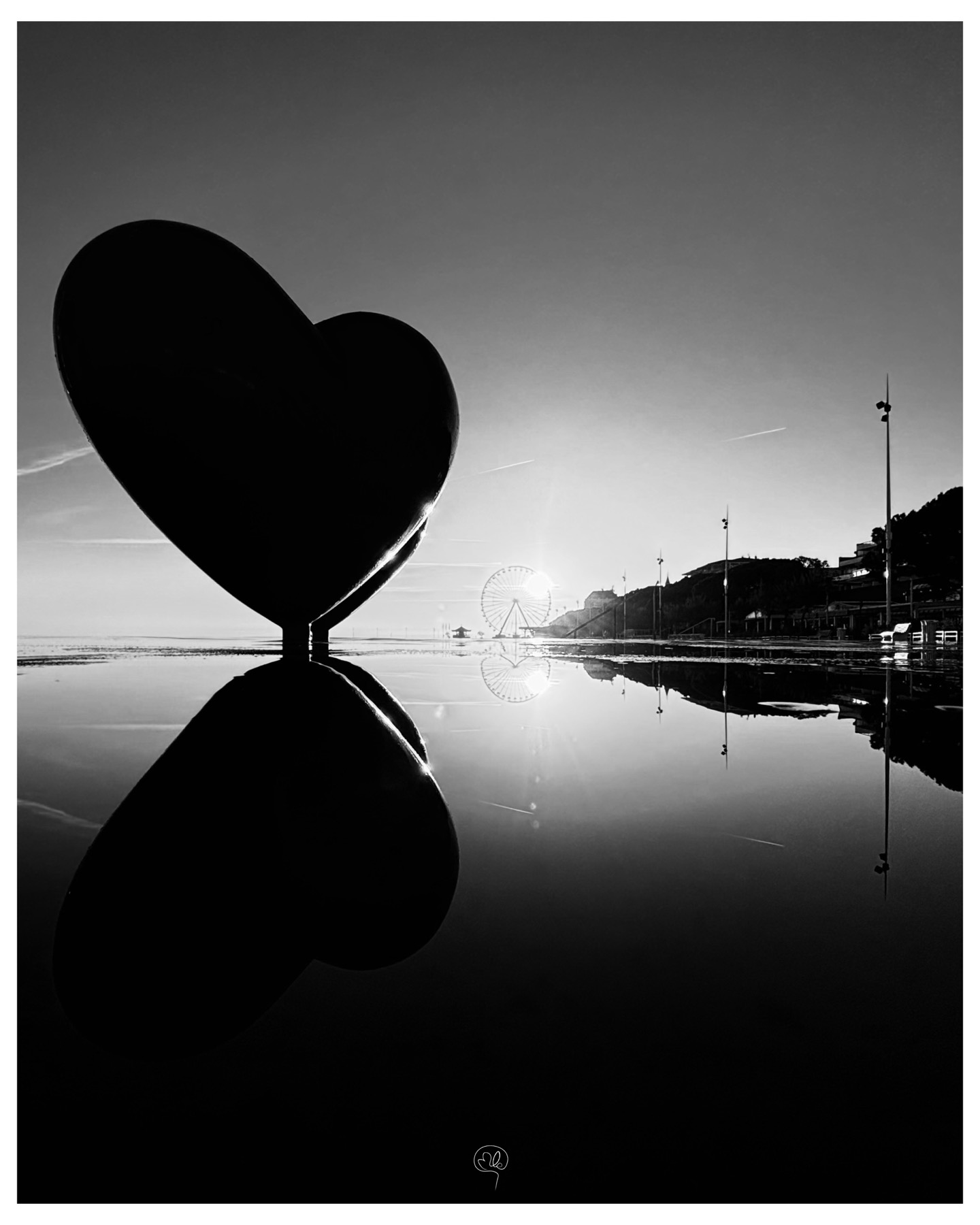 Heart-shaped sculpture, Ferris wheel and seafront reflected in a puddle