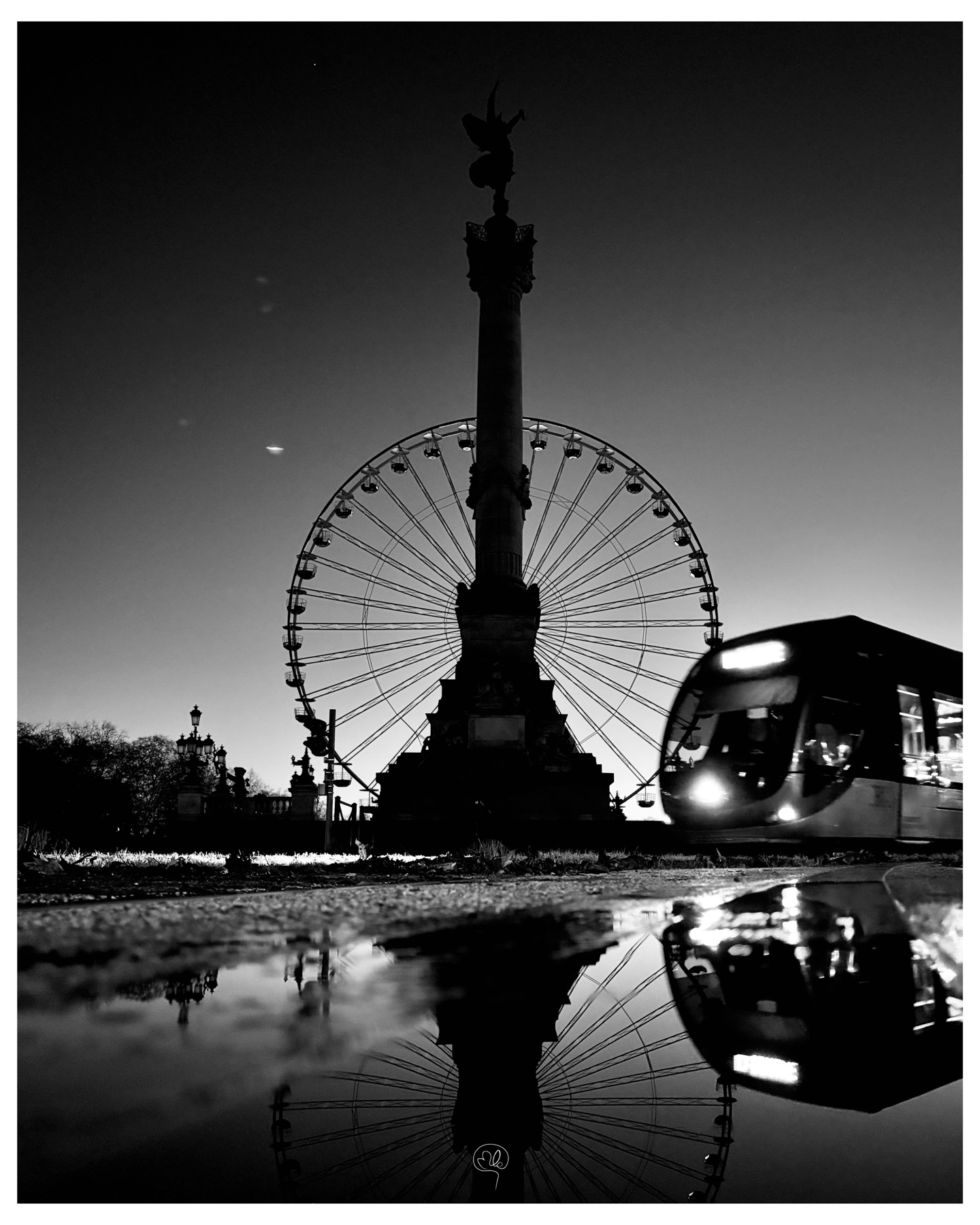 Ferris wheel, column and tram reflected in a nighttime puddle